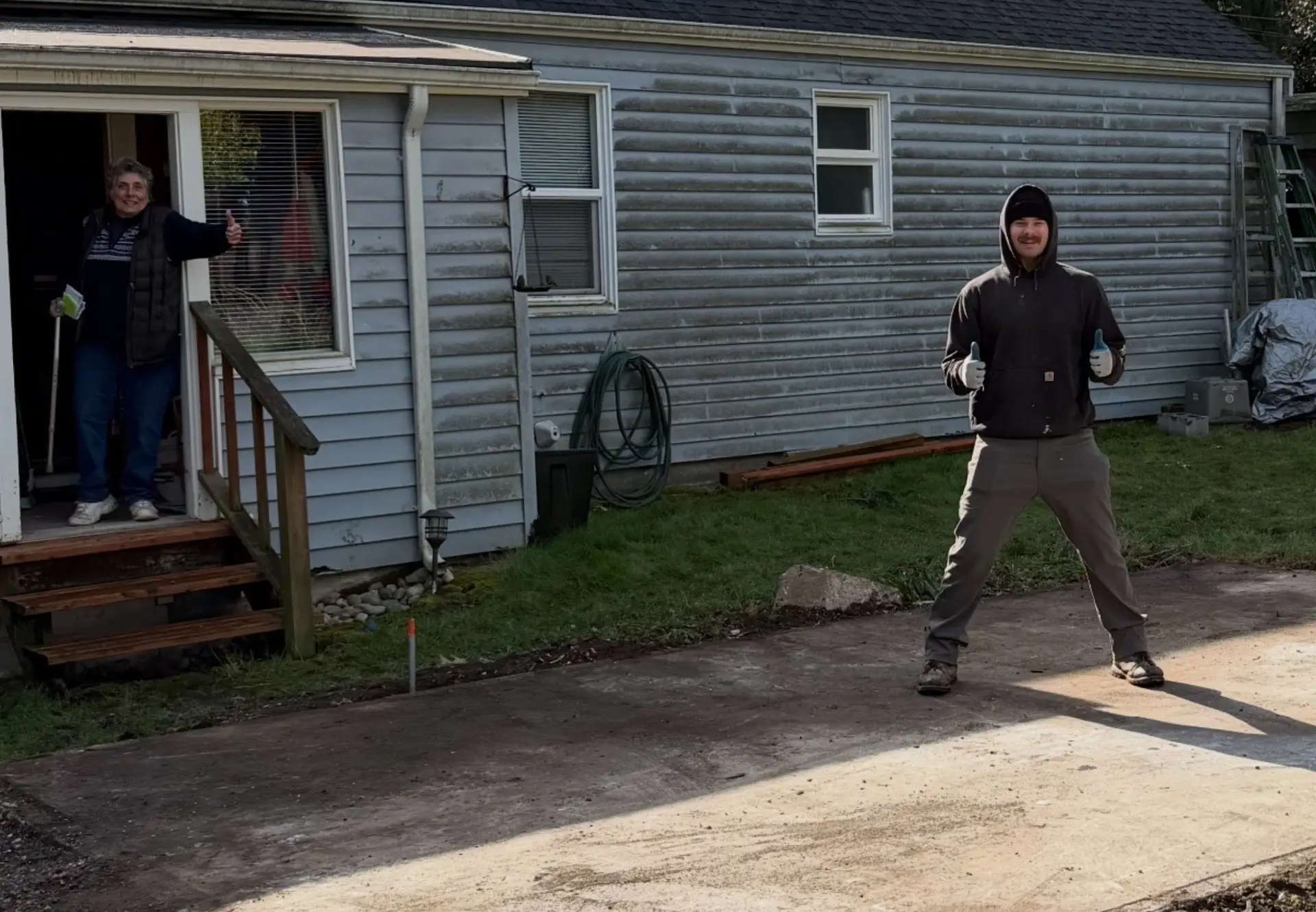 a man wearing a black hoodie and a woman in the door giving a big smile and a thumbs up